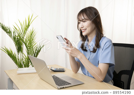 A woman holding a smartphone at the office and showing a smile A woman holding a smartphone at the office and showing a smile 89554190
