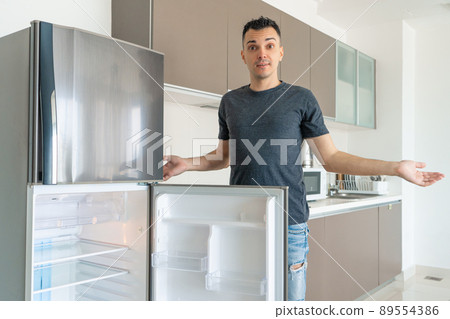 The guy is sad near the empty refrigerator without food. Food delivery service advertisement 89554386