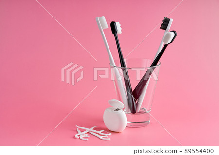 Fashionable toothbrush with soft bristles. Popular toothbrushes. Hygiene trends. Oral hygiene kit. Toothbrushes in glass, floss thread and toothpicks on a pink background Fashionable toothbrush with soft bristles. Popular toothbrushes. Hygiene trends. Oral hygiene kit. Toothbrushes in glass, floss thread and toothpicks on a pink background 89554400