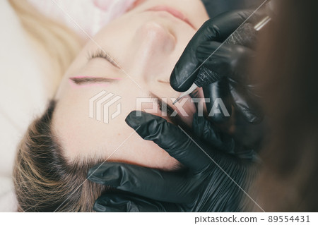 Cosmetologist applying permanent make up eyebrows for a client 89554431