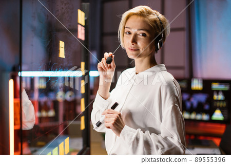 Caucasian woman in headset, posing near transparent glass board with marker pen 89555396