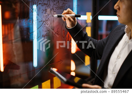 Close up cropped shot of businessman, writing notes on glass presentation board. Close up cropped shot of businessman, writing notes on glass presentation board. 89555467