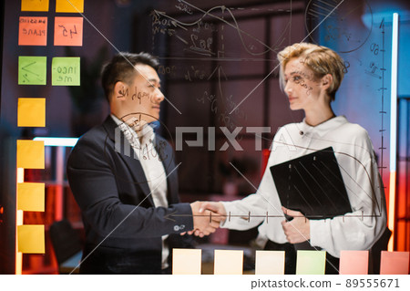 Male and female business colleagues, shaking hands after finishing up the meeting in modern office 89555671