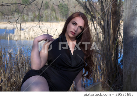 young woman in black dress sitting in the forest near water pond in sunshine 89555693
