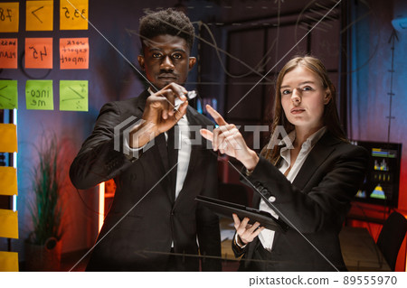 People in formal wear using adhesive notes and writing while standing behind the glass wall 89555970