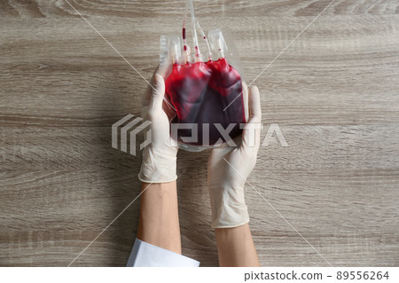 Woman holding blood for transfusion at wooden table, top view. Donation concept 89556264