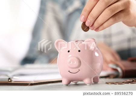 Woman putting money into piggy bank at table, closeup 89556270