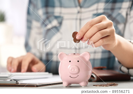 Woman putting money into piggy bank at table, closeup 89556271