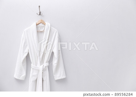 Fresh white bathrobe hanging on light wall. Space for text 89556284