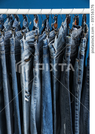 Rack with stylish jeans on blue background, closeup 89556376