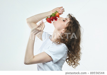 attractive girl is holding a skewer on which strawberries are strung. attractive girl is holding a skewer on which strawberries are strung. 89556544