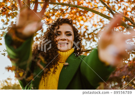 Girl pulls her hands into the camera smiling white-toothed charming smile against a backdrop of yellow tree leaves Girl pulls her hands into the camera smiling white-toothed charming smile against a backdrop of yellow tree leaves 89556789
