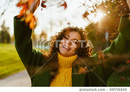 The curly-haired girl raised her hands to the leaves on the tree and smiles happily closing her eyes 89556848