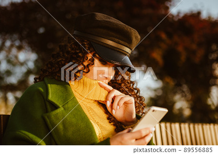 A girl in autumn clothes sits and looks at the phone 89556885