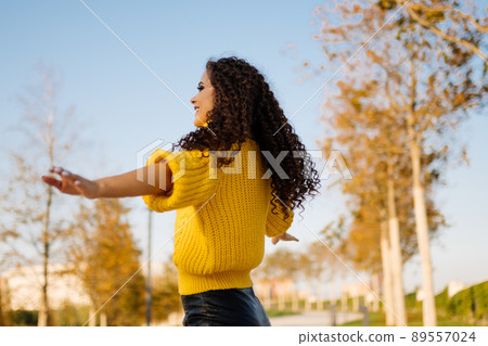 Curly brunette arms outstretched smiling sun in autumn park 89557024