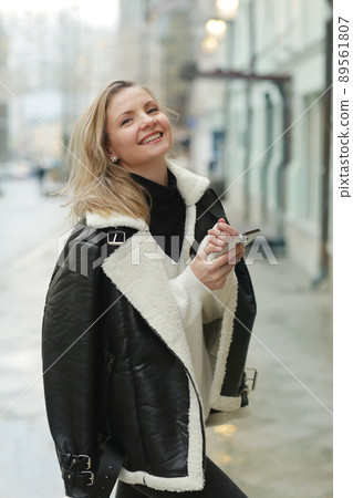 young blond slavic woman with cell phone in black leather jacket closeup street portrait young blond slavic woman with cell phone in black leather jacket closeup street portrait 89561807