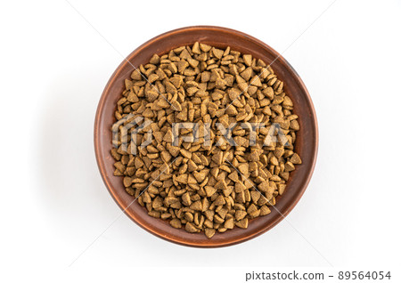 Pet food. Dry pelleted food in a brown clay bowl against a white background. The pellets are triangular in shape. 89564054