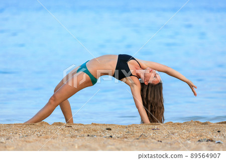 Young woman practicing yoga at the beach in the evening. Wild thing yoga pose against blue sea Young woman practicing yoga at the beach in the evening. Wild thing yoga pose against blue sea 89564907