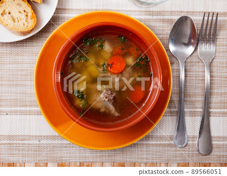 Soup in pork broth with potatoes, carrots, onions and herbs 89566051
