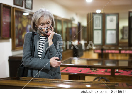 Pensive aged woman in protective mask exploring artworks in museum Pensive aged woman in protective mask exploring artworks in museum 89566153