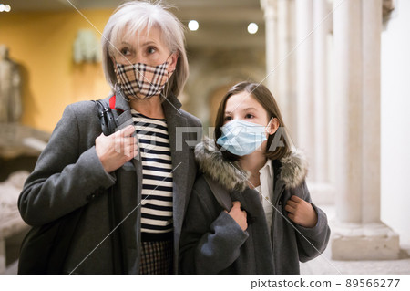 Elderly female tutor in protective mask showing tween girl ancient sculptures in museum Elderly female tutor in protective mask showing tween girl ancient sculptures in museum 89566277