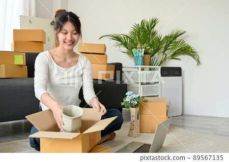Female online business owner enjoy packing her products into a parcel box. Female online business owner enjoy packing her products into a parcel box. 89567135