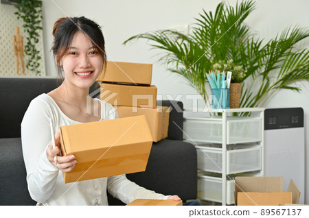 Female online shop owner packing her stuff in the living room Female online shop owner packing her stuff in the living room 89567137