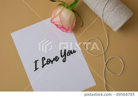 I LOVE YOU text on paper note. Delicate pink roses with spool of white cotton rope on beige background. Minimal trendy composition. Romantic pastel pink rose flowers. Neutral earth tones. Greeting I LOVE YOU text on paper note. Delicate pink roses with spool of white cotton rope on beige background. Minimal trendy composition. Romantic pastel pink rose flowers. Neutral earth tones. Greeting 89568785