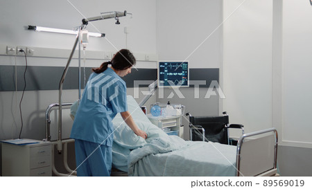 Medical assistant preparing hospital ward bed for patient at facility. Woman working as nurse getting intensive care room ready for healthcare treatment and recovery of sick person Medical assistant preparing hospital ward bed for patient at facility. Woman working as nurse getting intensive care room ready for healthcare treatment and recovery of sick person 89569019