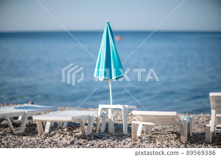 Several white sun loungers and a turquoise parasol on a deserted beach. The perfect vacation concept. Several white sun loungers and a turquoise parasol on a deserted beach. The perfect vacation concept. 89569386