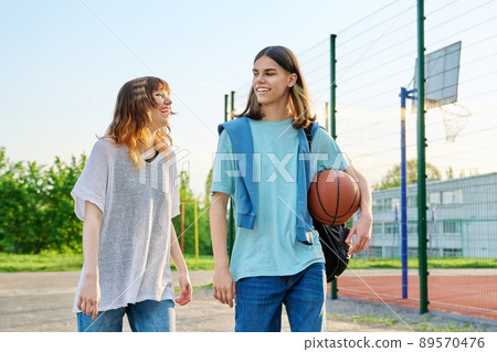 Young teenage male female students with ball walking outdoor near basketball court Young teenage male female students with ball walking outdoor near basketball court 89570476