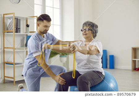 Physiotherapist helping senior woman with osteoporosis to do exercises on fitball 89570679