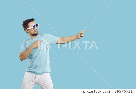 Young cheerful man points fingers at blank copy space on vivid light blue background. 89570731