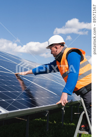 Solar power plant worker on stepladder makes a visual inspection of solar panels Solar power plant worker on stepladder makes a visual inspection of solar panels 89571567