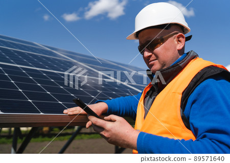 Man in hard hat using smartphone on the background of solar panels 89571640