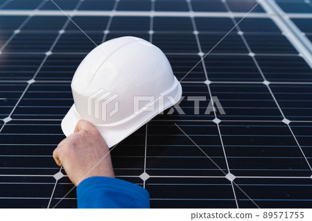Hand of the engineer takes the helmet that lies on the solar panel. Alternative energy concept. Hand of the engineer takes the helmet that lies on the solar panel. Alternative energy concept. 89571755
