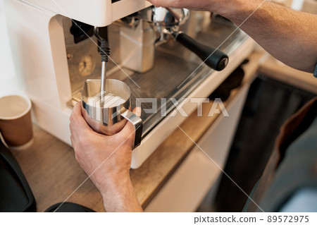Close up of barista hands heating up milk in pitcher with steam Close up of barista hands heating up milk in pitcher with steam 89572975
