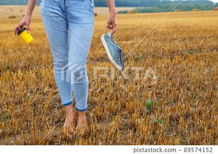 barefoot girl with sneakers and cardboard cup with coffee in hand stand in the agricultural field barefoot girl with sneakers and cardboard cup with coffee in hand stand in the agricultural field 89574152
