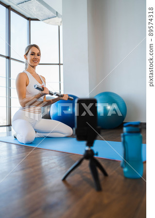 Female fitness trainer with dumbbells in his hands records his video lessons on a smartphone Female fitness trainer with dumbbells in his hands records his video lessons on a smartphone 89574318