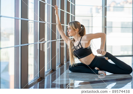 Sporty yoga girl in pigeon pose. Woman in black sportswear doing stretching 89574438
