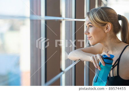 Smiling fitness girl with sports bottle looking out the window 89574455