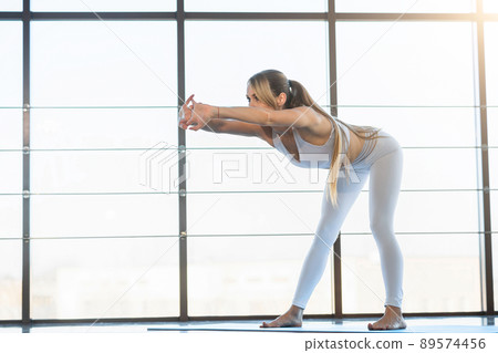 Beautiful girl in white sportswear warms up against the background of panoramic windows Beautiful girl in white sportswear warms up against the background of panoramic windows 89574456