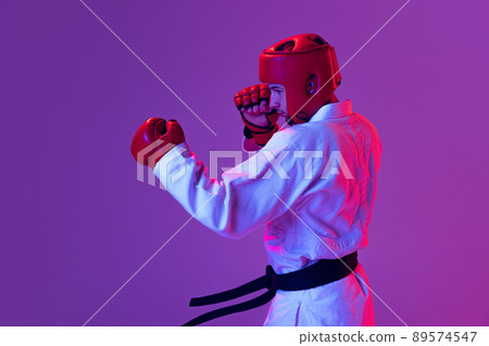 Studio shot of male taekwondo fighter in sports uniform in action isolated over purple background in neon light. Concept of sport, workout, competition, ad 89574547