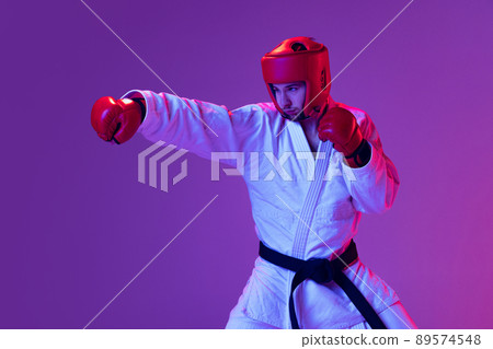 Studio shot of male taekwondo fighter in sports uniform in action isolated over purple background in neon light. Concept of sport, workout, competition, ad 89574548