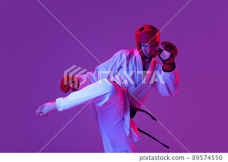 Studio shot of male taekwondo fighter in sports uniform in action isolated over purple background in neon light. Concept of sport, workout, competition, ad 89574550