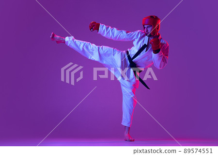 Studio shot of male taekwondo fighter in sports uniform in action isolated over purple background in neon light. Concept of sport, workout, competition, ad 89574551