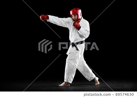 Male taekwondo fighter in white dobok, helmet and gloves training isolated over dark background. Concept of sport, workout, competition, ad 89574630