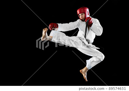 Male taekwondo fighter in white dobok, helmet and gloves training isolated over dark background. Concept of sport, workout, competition, ad 89574631