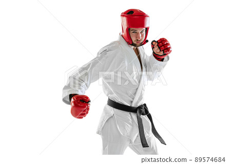 Portrait of young sportive man wearing white dobok, helmet and gloves practicing isolated over white background. Concept of sport, workout, health. 89574684