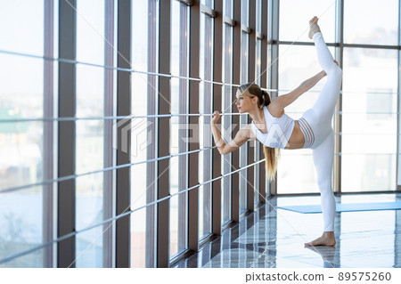 Fitness girl practicing twine. .Flexible woman in the gymnastics room stretches by the panoramic window 89575260